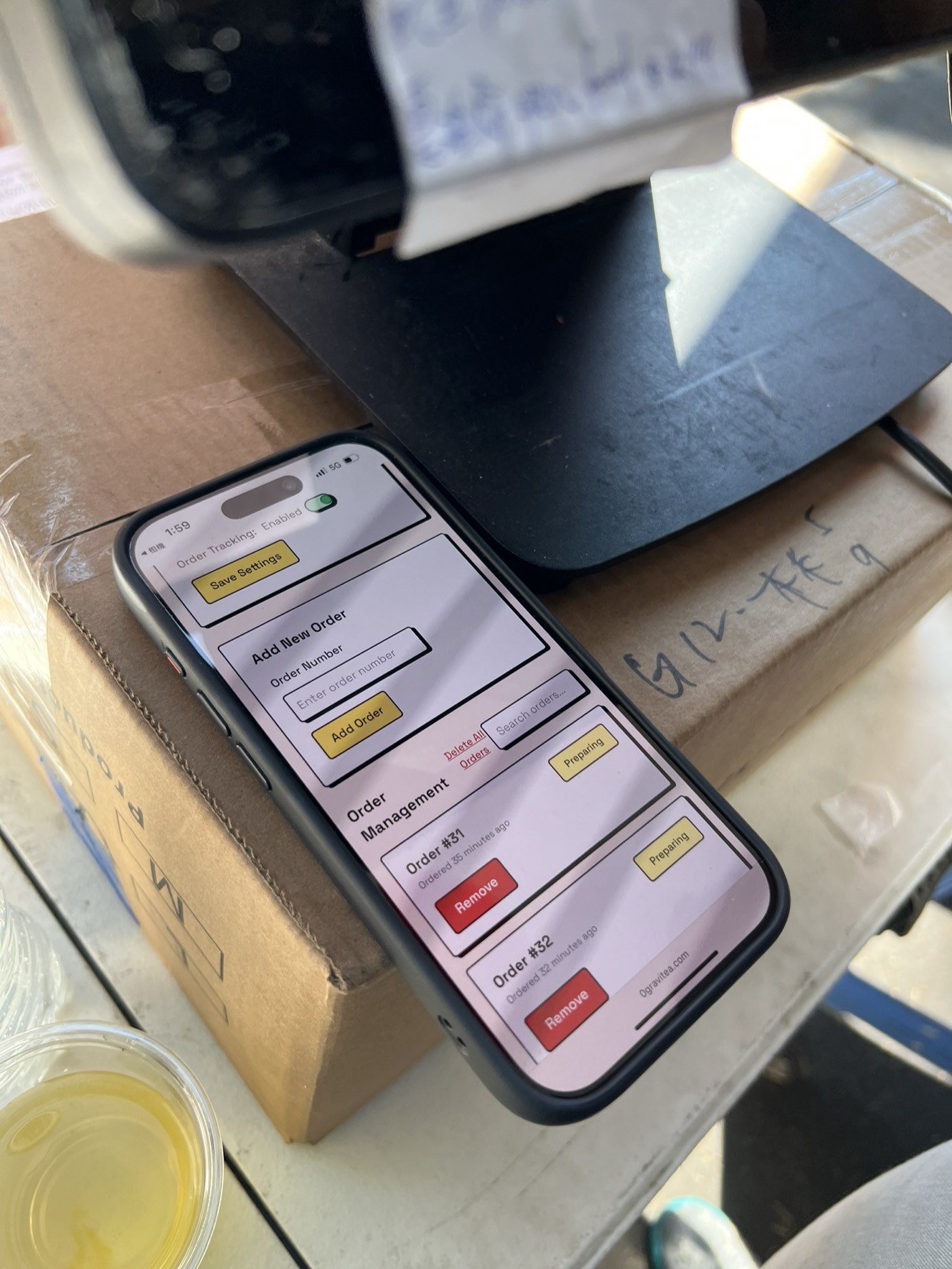 The order tracker admin page open on an iPhone at the food truck, showing an add-order form and a list of orders with status and remove buttons.